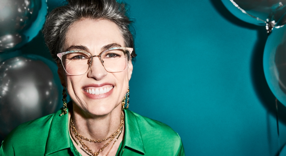 Person wearing translucent, light pink eyeglasses with gold accents and a green shirt, smiling brightly.