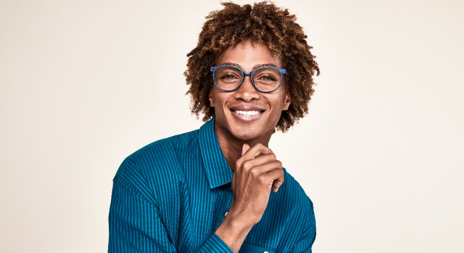 Person smiling while wearing blue-rimmed eyeglasses and a turquoise shirt.