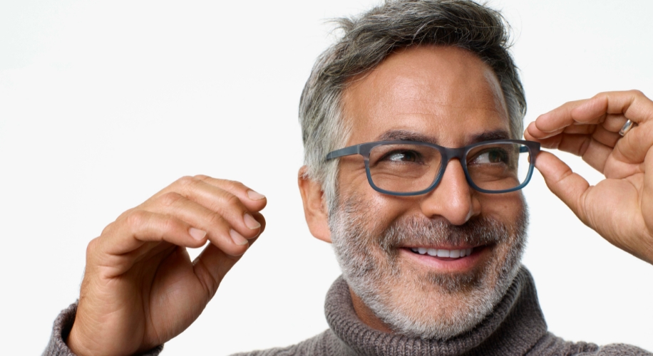 Man smiling while adjusting black frame glasses.