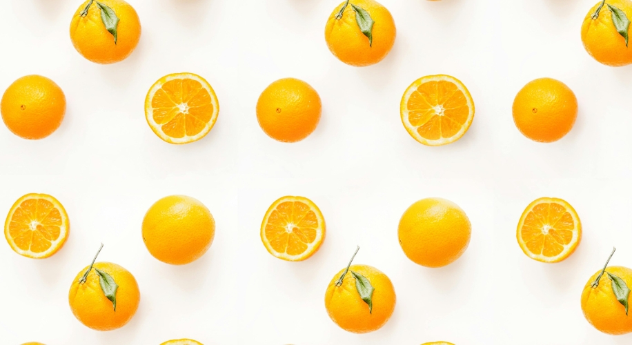 Whole and halved oranges with green leaves arranged in a repeating pattern.