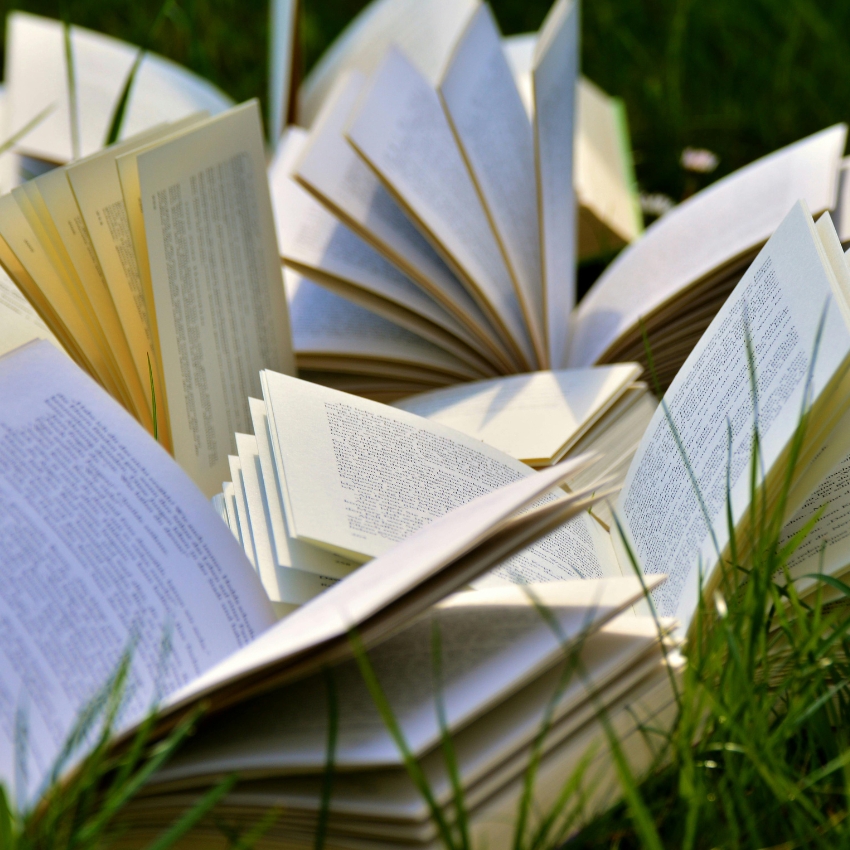 Open books with pages fanned out, lying on grass.