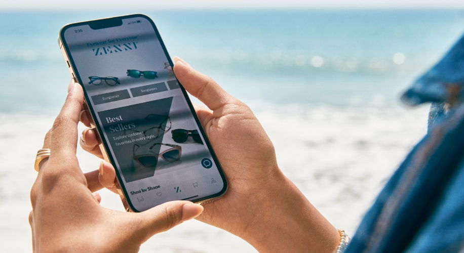 Smartphone displaying an eyewear app with categories: Eyeglasses, Sunglasses. Text: &quot;Eyewear for Everyone. ZENNI,&quot; &quot;Best Sellers. Explore customer favorites in every style.,&quot; &quot;Shop by Shape.&quot;