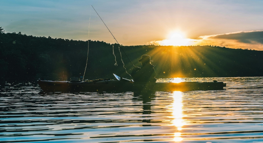 Person fishing in a kayak on a lake at sunset.