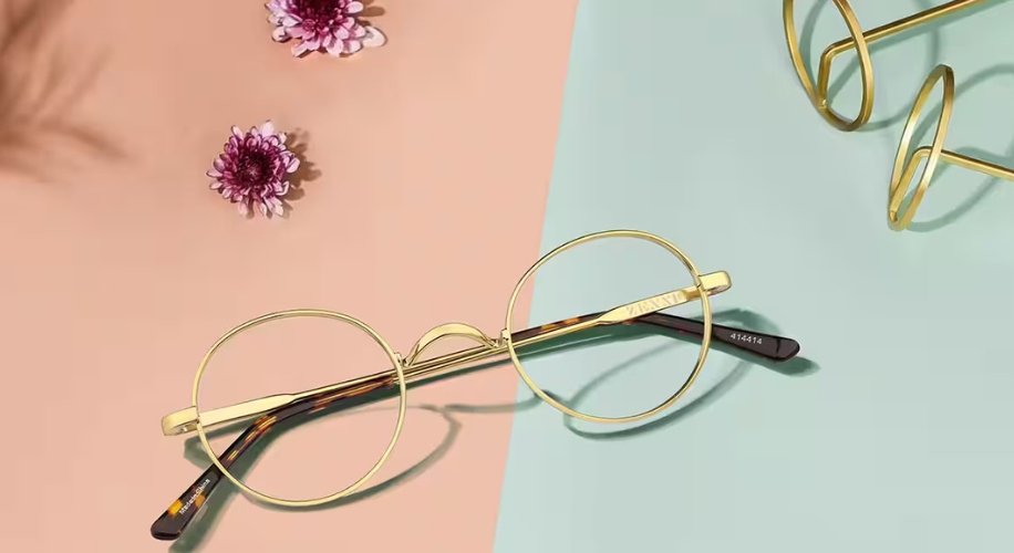 Round gold wire eyeglasses with tortoiseshell temple tips on a pastel background with flowers.