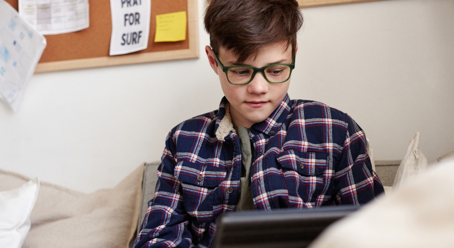 A child wearing green-framed glasses and a plaid shirt uses a tablet.