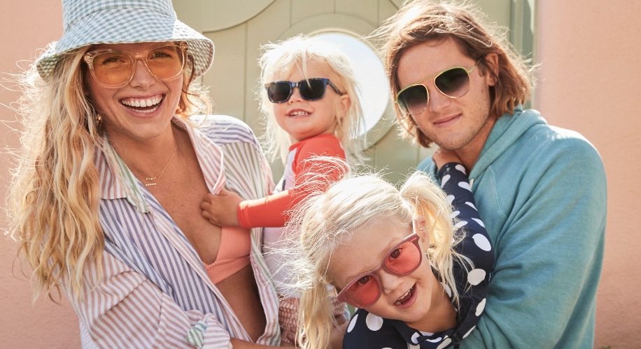 Smiling family wearing sunglasses; mother in orange sunglasses, father in green, children in black and pink.