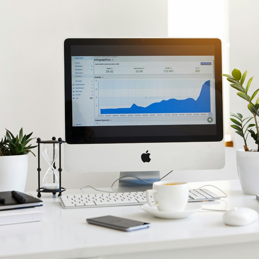 Apple desktop displaying an infographic with a graph showing growth, surrounded by a keyboard, mouse, and plants on the desk.