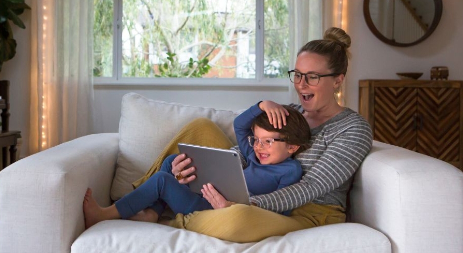 Woman and child sitting on a couch, smiling and looking at a tablet together.