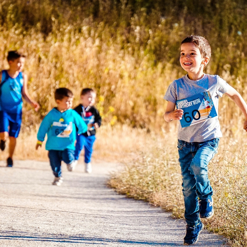 Children running on a trail wearing race bibs. Bib text: "SAMUEL'S BIRTHDAY RUN" with numbers 60, 62.