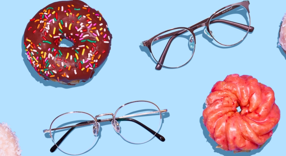 Two pairs of eyeglasses, one with a thin silver frame and one with a thicker brown frame, surrounded by donuts.