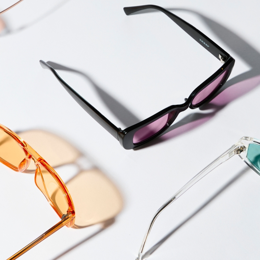 Three pairs of sunglasses: Black frame with purple lenses, orange frame with tinted lenses, clear frame with blue lenses.
