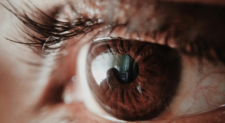Close-up of a brown eye with detailed reflection of an indoor scene in the pupil.