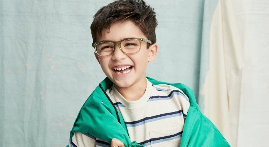 Smiling boy wearing green glasses, a white and blue striped shirt, and a green jacket.