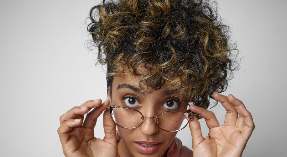 Woman wearing round eyeglasses with thin, metal frames, holding the glasses with both hands.
