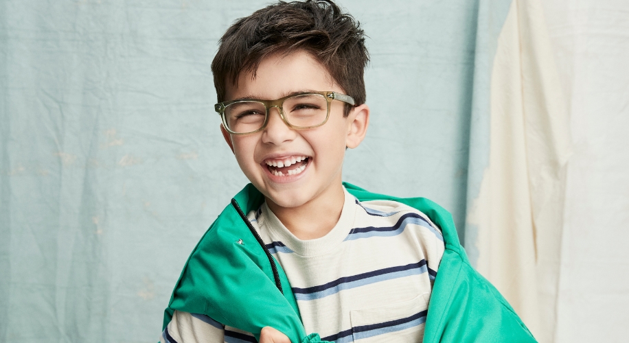 Child wearing green eyeglasses and a green jacket over a striped shirt.