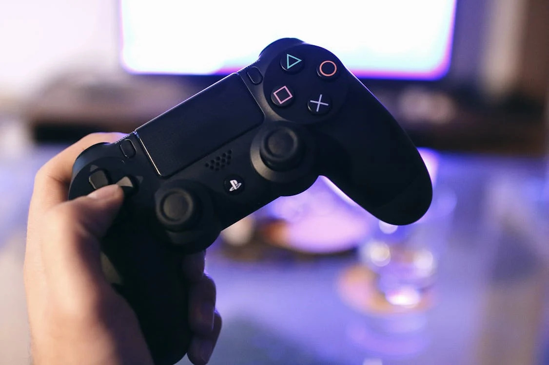 Person holding a black PlayStation controller with PlayStation symbols on buttons.