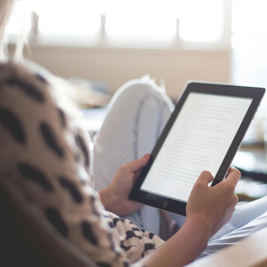 Person reading an e-book on a tablet while resting indoors.