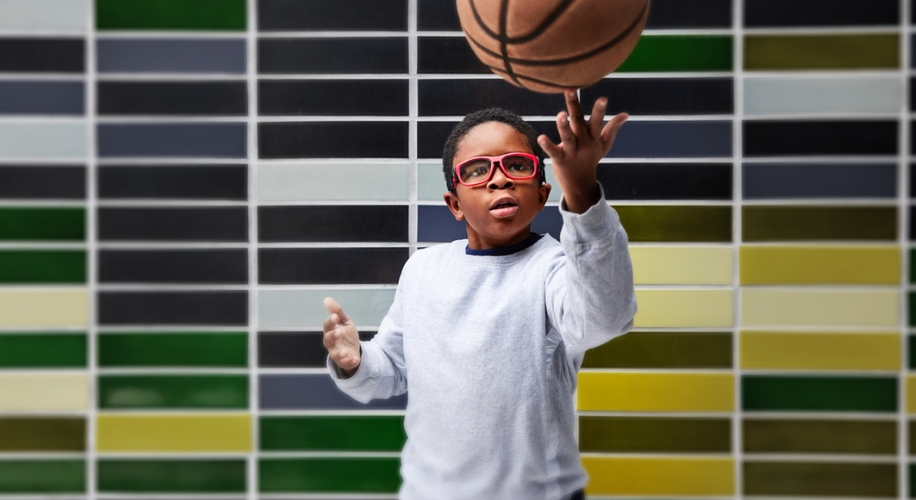 Child wearing red-framed glasses catching a basketball.