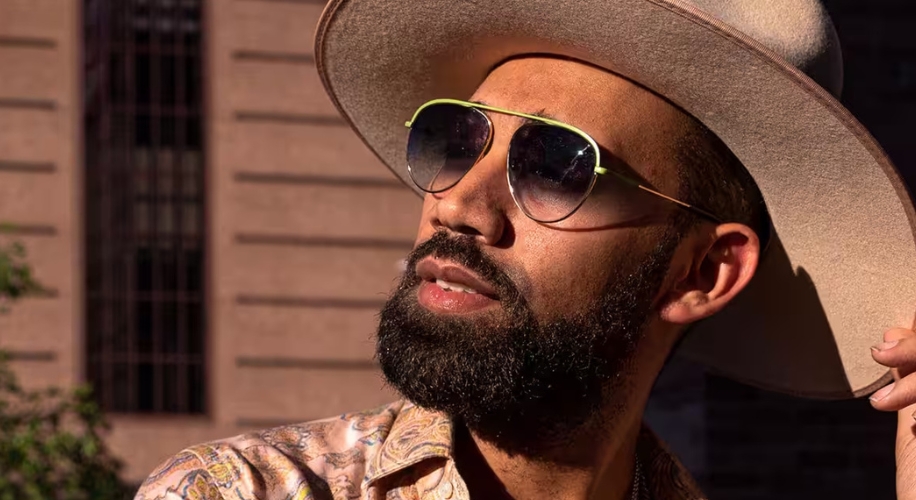 Man wearing wide-brimmed hat, aviator sunglasses, and patterned shirt.