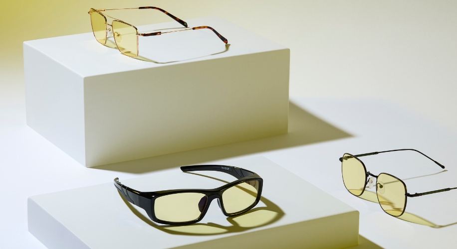 Three pairs of yellow-tinted glasses on white display stands; each with different frame styles.