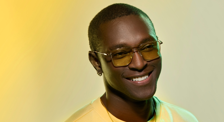 Man wearing yellow-tinted eyeglasses and a light-colored shirt, smiling.