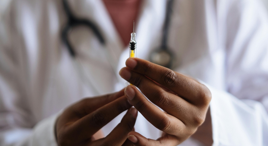 A person holding a filled syringe with both hands, wearing a white lab coat and a stethoscope.