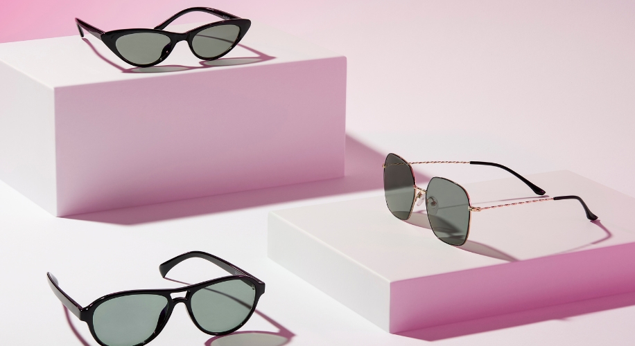 Three pairs of sunglasses with different designs displayed on white platforms against a pink background.