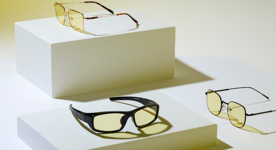 Three pairs of glasses with yellow tinted lenses displayed on white stands.