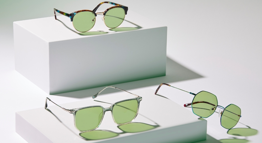 Three pairs of green-lensed sunglasses with different frame styles displayed on white platforms.