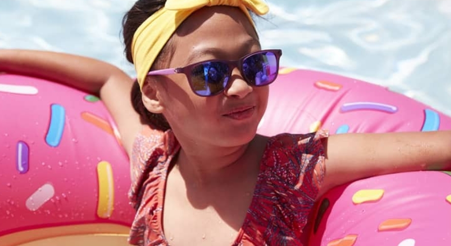 Child in a donut-shaped inflatable pool float, wearing a yellow headband, sunglasses, and a red swimsuit.