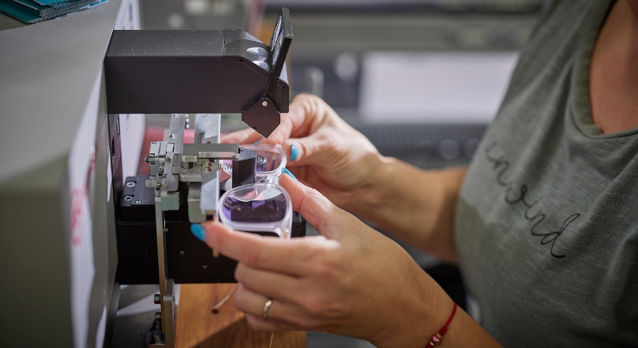 Hands holding eyeglasses under a lens shaping machine.