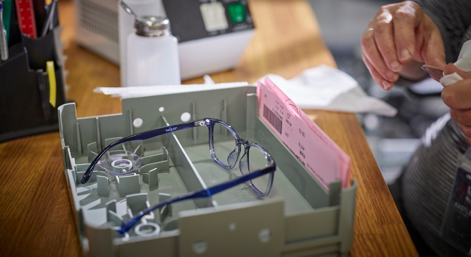 Eyeglasses in a gray tray with pink label and prescription details.