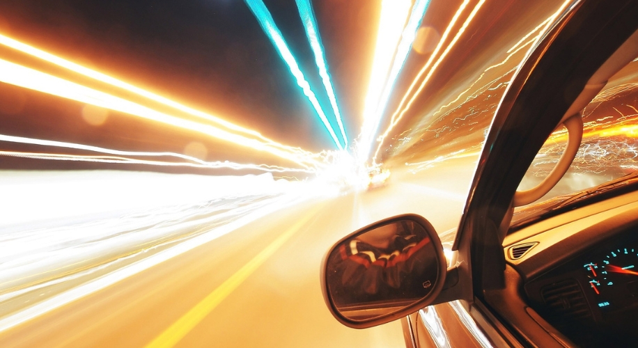 Driving at high speed with light trails and a view of the car&#039;s side mirror and dashboard.