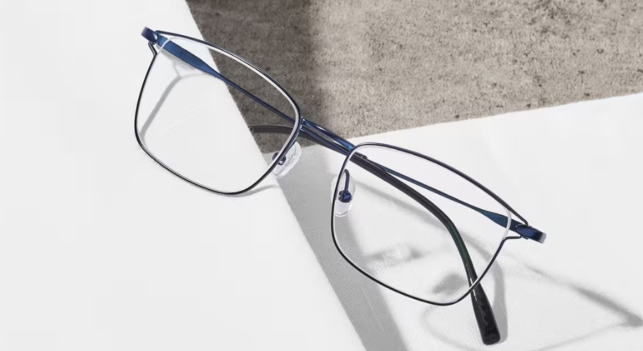 Thin, rectangular-framed eyeglasses with nose pads and dark blue metal arms on a white and grey surface.