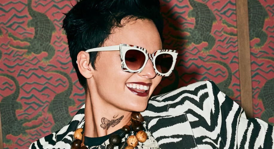 Woman wearing white and black zebra-patterned sunglasses and matching blazer, smiling.