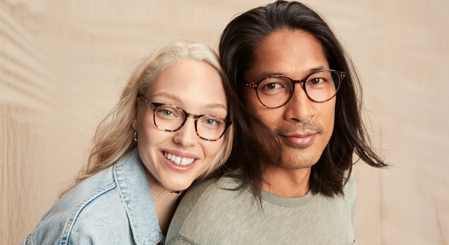 Man and woman wearing stylish, round, and rectangular eyeglasses smiling at the camera.