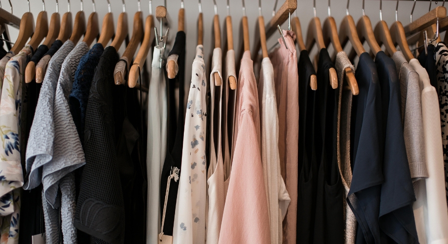 Various clothing items on wooden hangers, including dresses, tops, and sweaters in different colors and patterns.