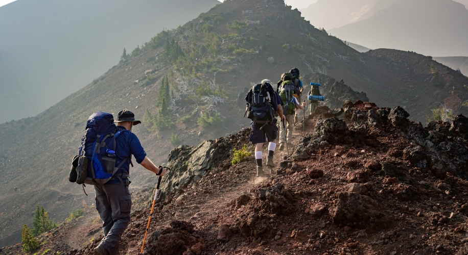 Hikers with large backpacks and trekking poles climbing a rocky mountain trail.