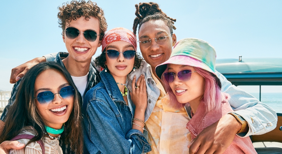 Group of friends wearing stylish sunglasses and smiles, showcasing diverse sunglass designs in vibrant colors.