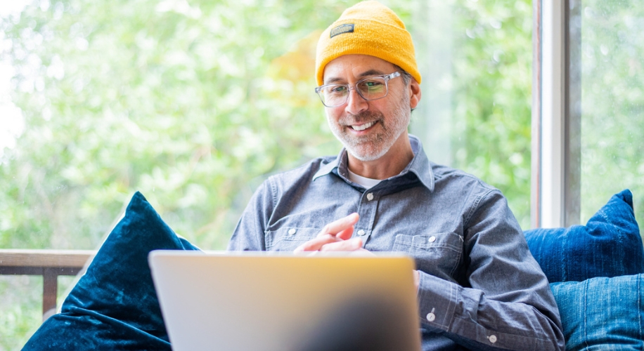Man wearing a yellow beanie and gray shirt using a laptop.