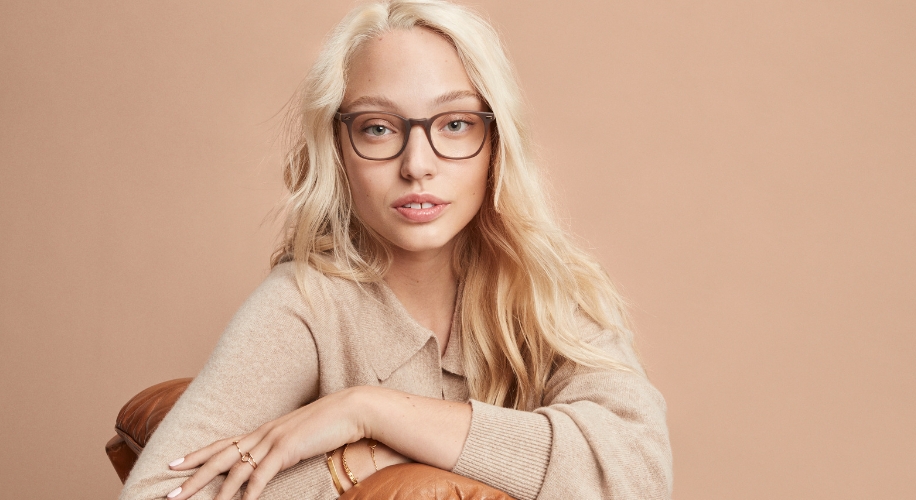 Woman wearing brown-framed eyeglasses, beige sweater, and gold rings and bracelet.