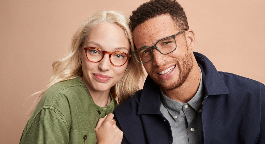 Two people wearing stylish eyeglasses, one with thin red frames and the other with dark green frames.