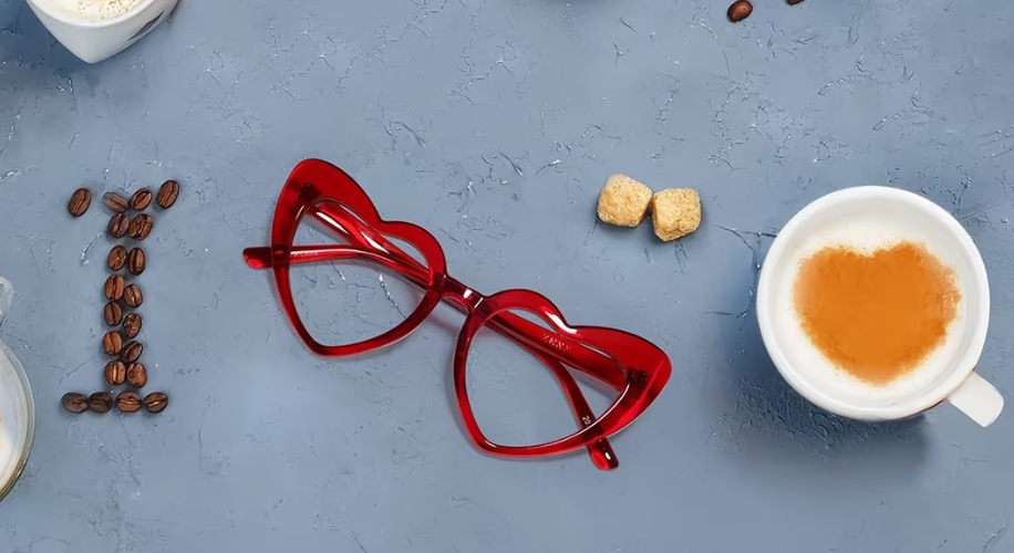 Red, heart-shaped glasses next to a cappuccino with a heart latte art, coffee beans forming &quot;I&quot;.