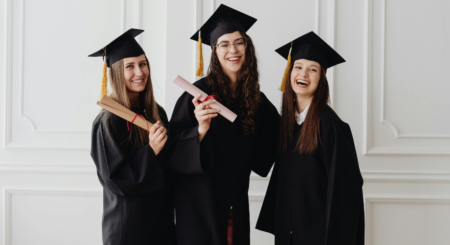 Three graduates in caps and gowns holding diplomas and smiling.