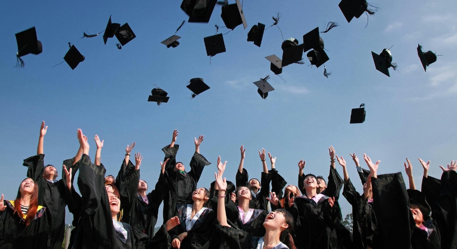 Graduates in academic robes throwing caps into the air, celebrating their graduation.