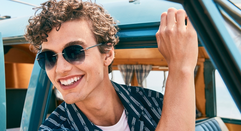 Man wearing dark aviator sunglasses with a slight smile, gazing slightly off-camera.