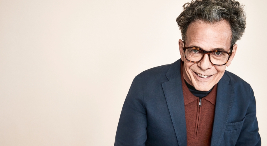 Man wearing glasses, a navy blazer, and a rust-colored zip-up shirt.