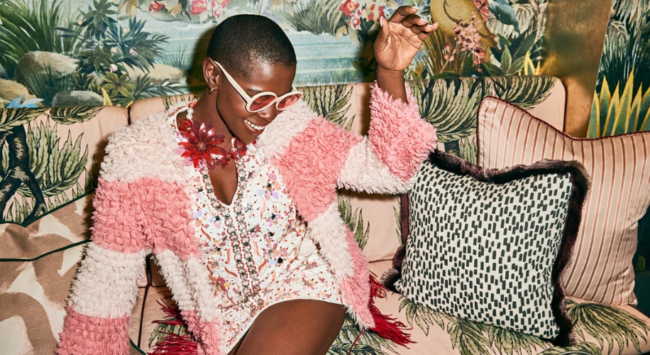 Person wearing sunglasses and a pink and white fluffy jacket over a white, sequin-embellished dress.