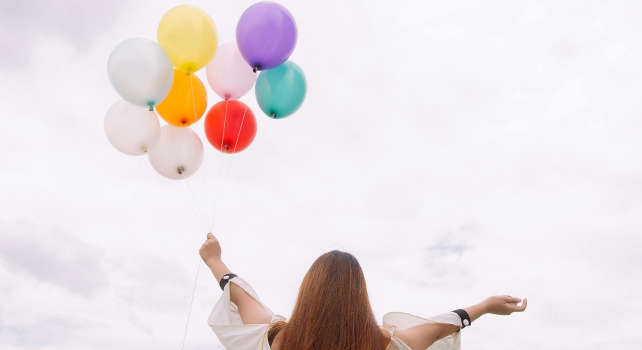 Person holding colorful balloons against a cloudy sky.