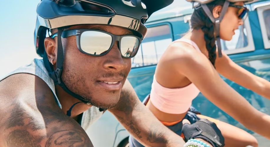 Cyclists wearing sunglasses and black helmets, with a focus on the sunglasses&#039; reflective lenses.